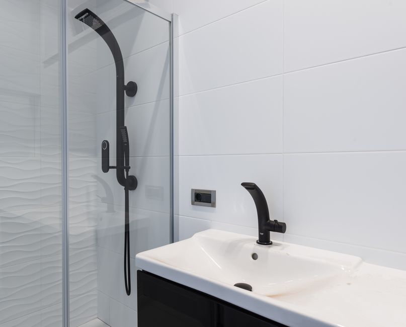 Modern minimalist style interior design of bathroom with white tiled walls and washbasin and black faucet and shower unit with glass partition. Photo by Max Vakhtbovych on Pexels