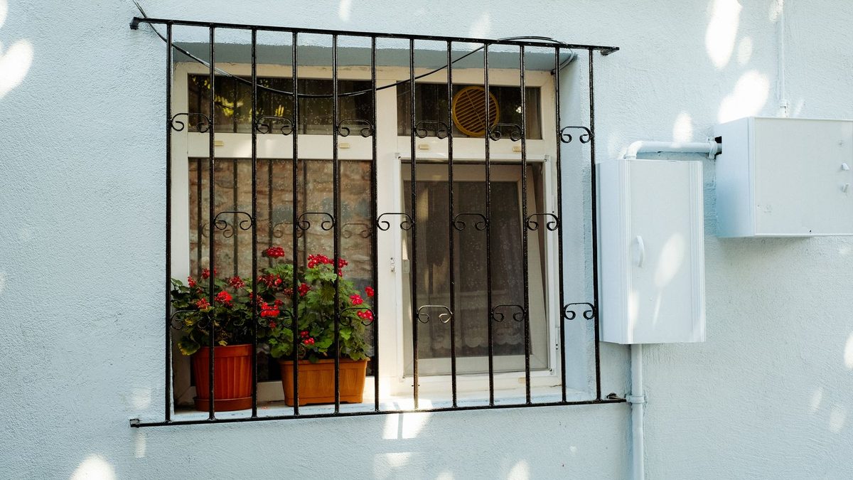 White apartment window with metal grille and flower pots. Photo by Mathias Reding on Pexels