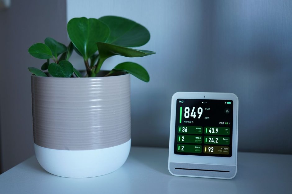 Indoor air quality monitor showing humidity readings beside a potted plant. Photo by Tim Witzdam on Pexels