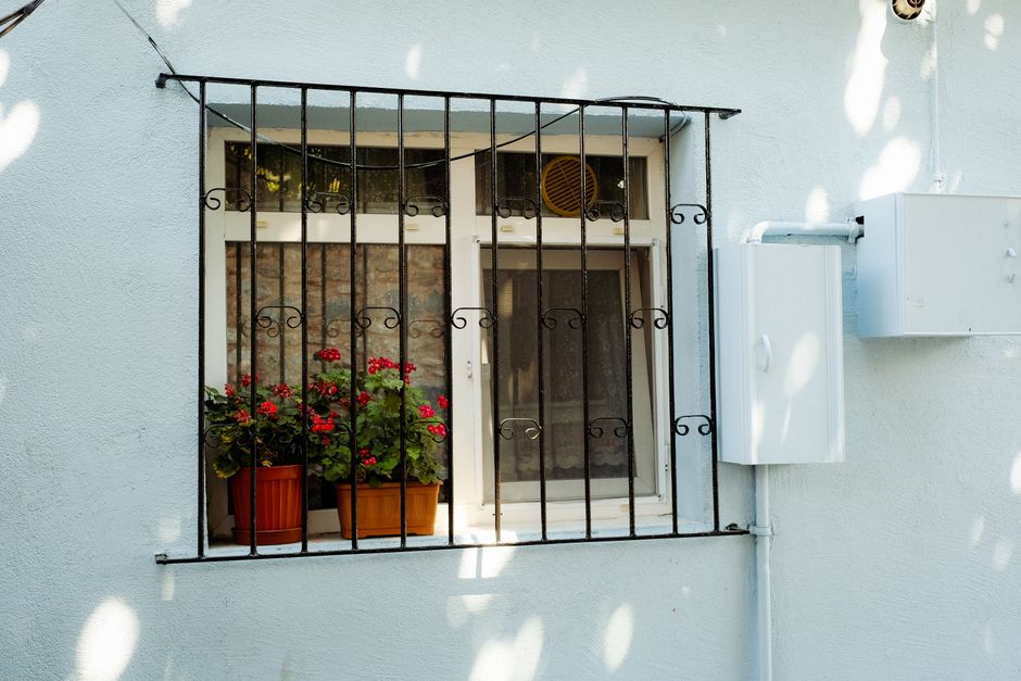 A charming window with potted red geraniums behind a decorative iron grill. Photo by Mathias Reding on Pexels