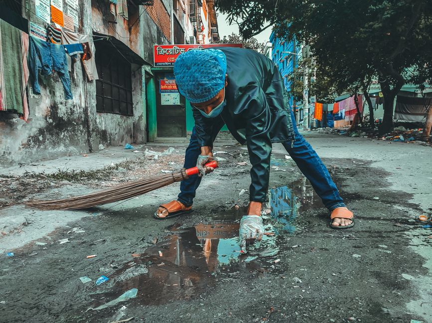 A person wearing a mask and gloves cleaning the street in a Bangladesh neighborhood. Photo by Rakib Farabi on Pexels