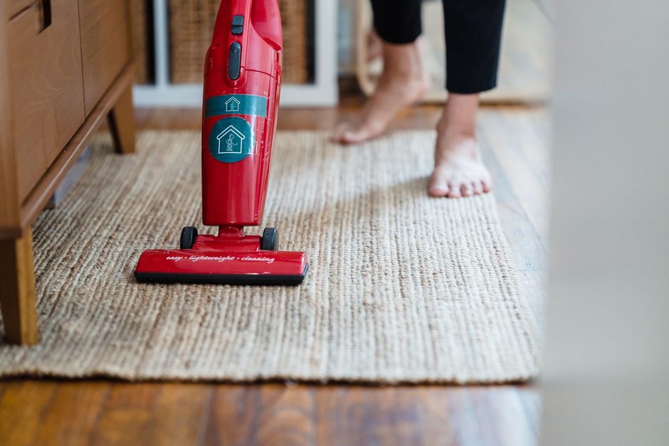 Red handheld vacuum cleaning a woven rug on a wooden floor. Photo by Liliana Drew on Pexels