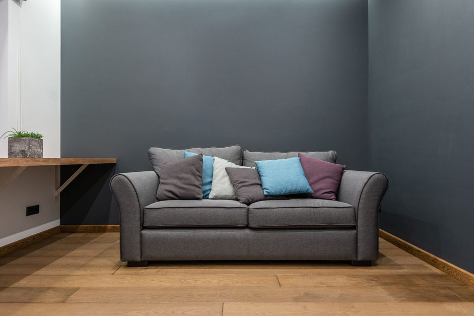 Grey fabric sofa with colourful cushions against a dark wall in a living room. Photo by Max Vakhtbovych on Pexels