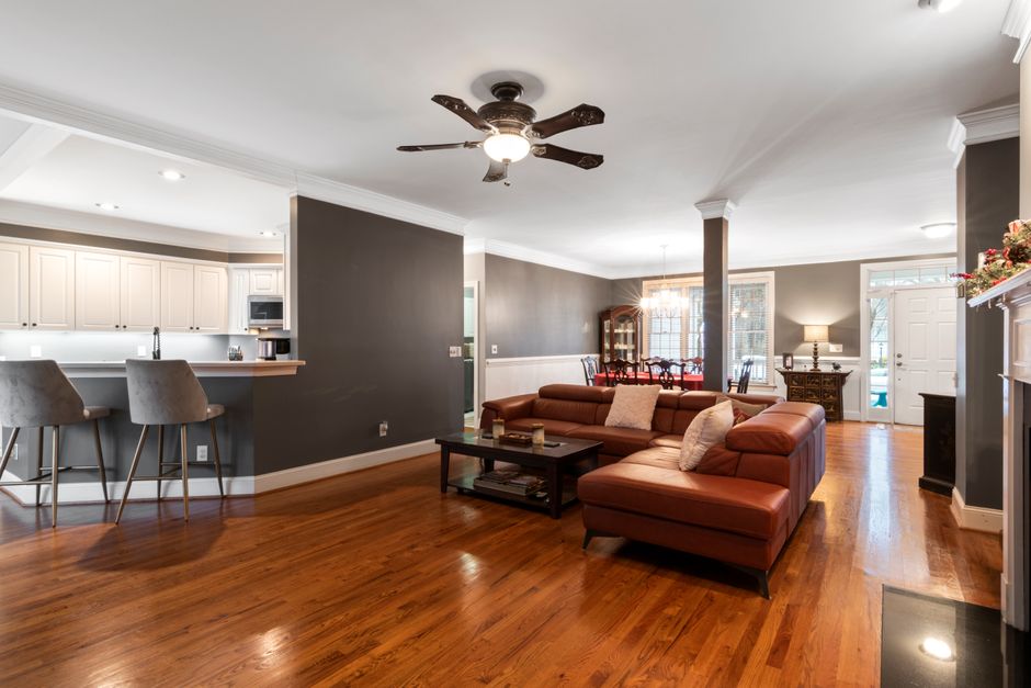 Photo by Curtis Adams on Pexels Elegant living room with modern leather sofa, ceiling fan, and open kitchen area.