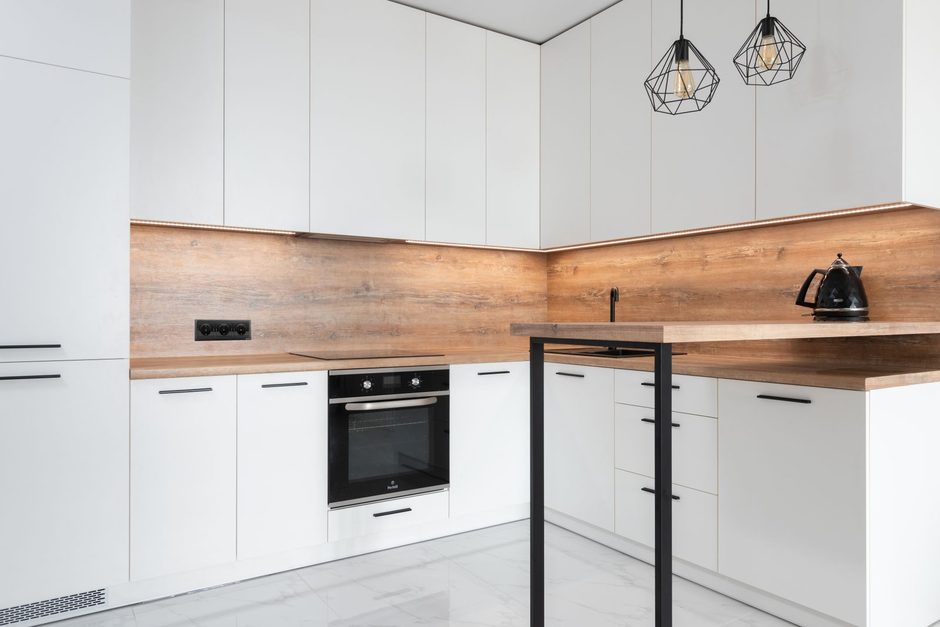 Modern white kitchen with new cabinets, built-in oven and wood backsplash in a renovated home. Photo by Max Vakhtbovych on Pexels