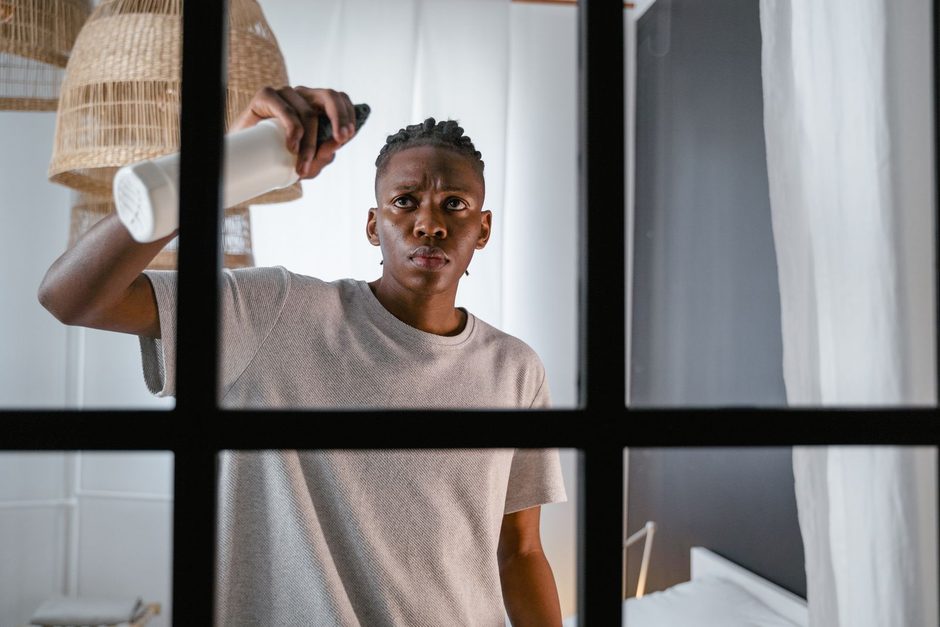 Man spraying and wiping a black-framed window in a bright room. Photo by MART  PRODUCTION on Pexels