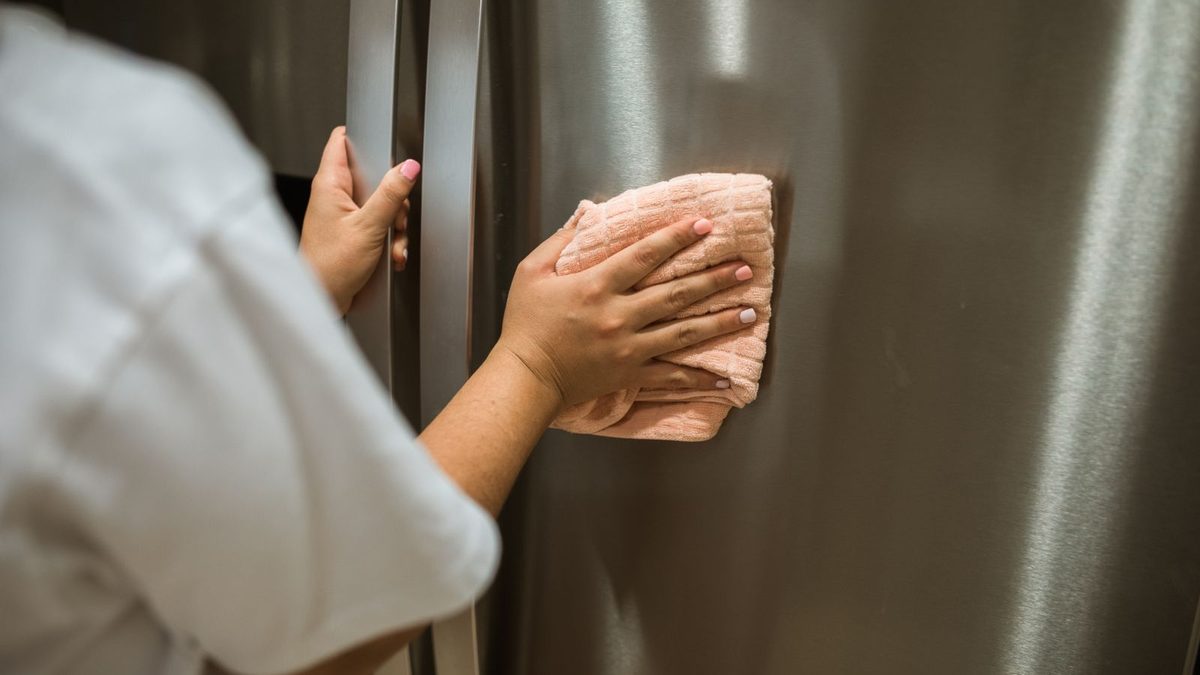 Hand wiping a stainless steel fridge door with a cloth in a modern kitchen. Photo by RDNE Stock project on Pexels