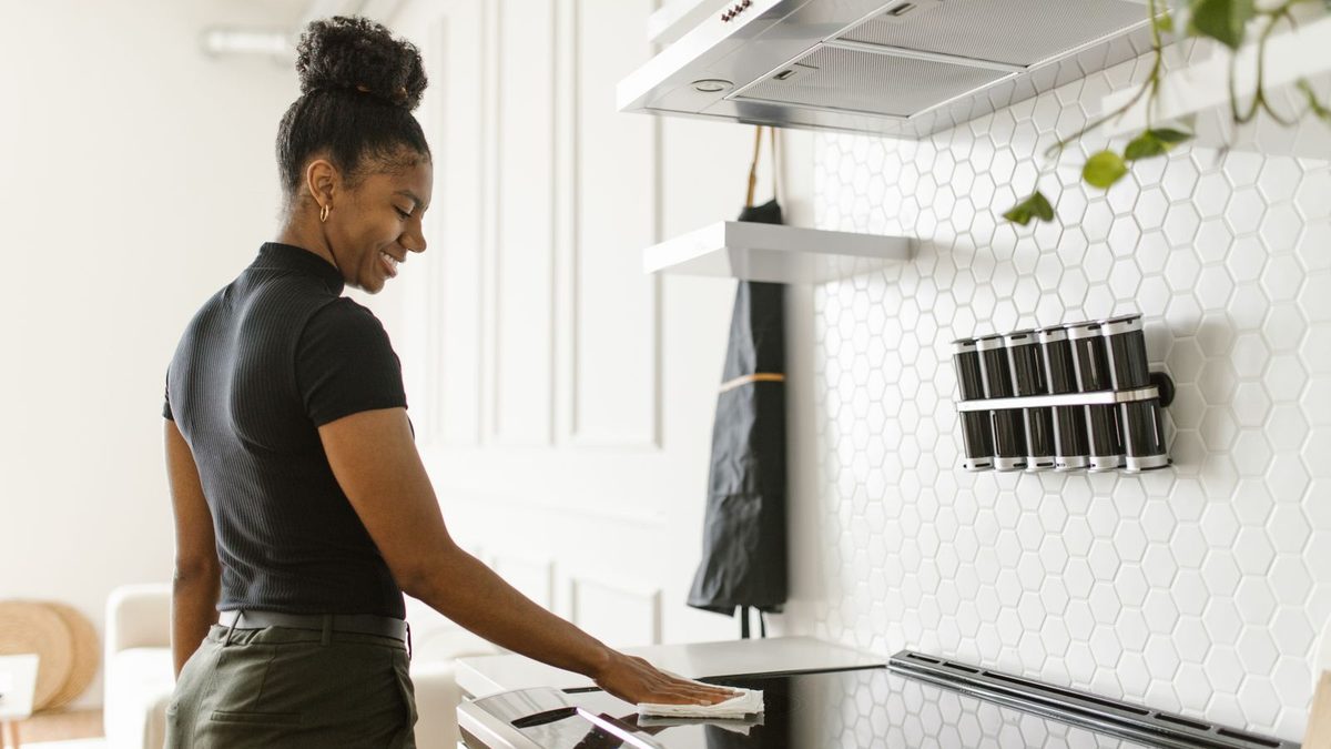 Woman cleaning the cooktop in a bright white kitchen with extractor hood. Photo by RDNE Stock project on Pexels