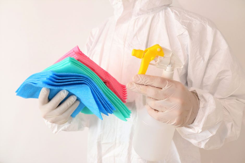 Photo by Roger Brown on Pexels Individual in PPE holds cleaning cloths and spray bottle, ensuring hygiene and safety. - Photo by Roger Brown on Pexels