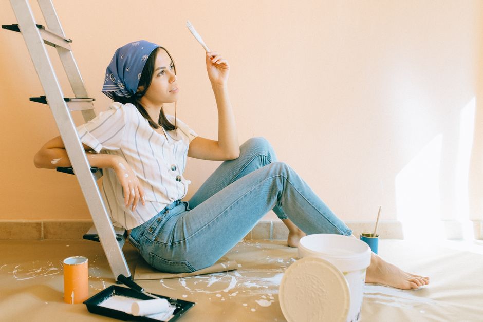 Photo by Nataliya Vaitkevich on Pexels A woman sits barefoot in a room, holding a paintbrush, leaning against a ladder. - Photo by Nataliya Vaitkevich on Pexels