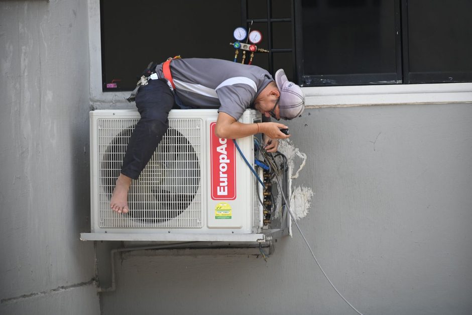 Photo by Richard Low Hong on Pexels Technician cleaning an air conditioner unit mounted on an apartment building wall. Photo by Richard Low Hong on Pexels