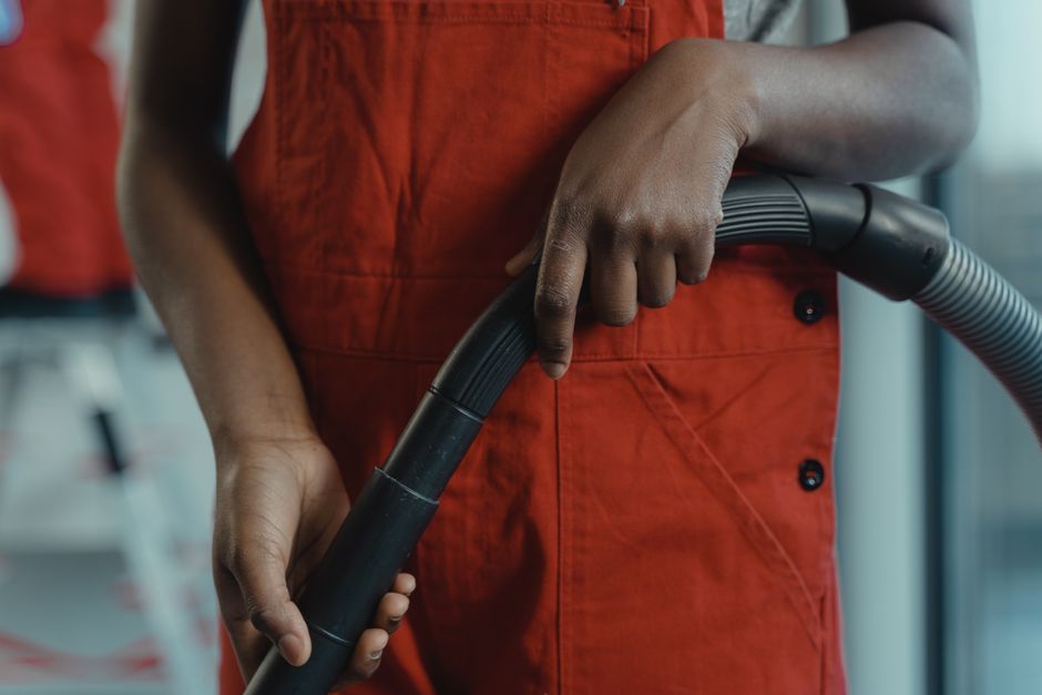 Photo by Tima Miroshnichenko on Pexels A person in a red apron holding a vacuum cleaner hose during indoor cleaning. - Photo by Tima Miroshnichenko on Pexels