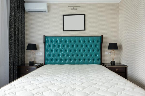 Mattress on bed with upholstery between lamps on bedside tables under air conditioning in house