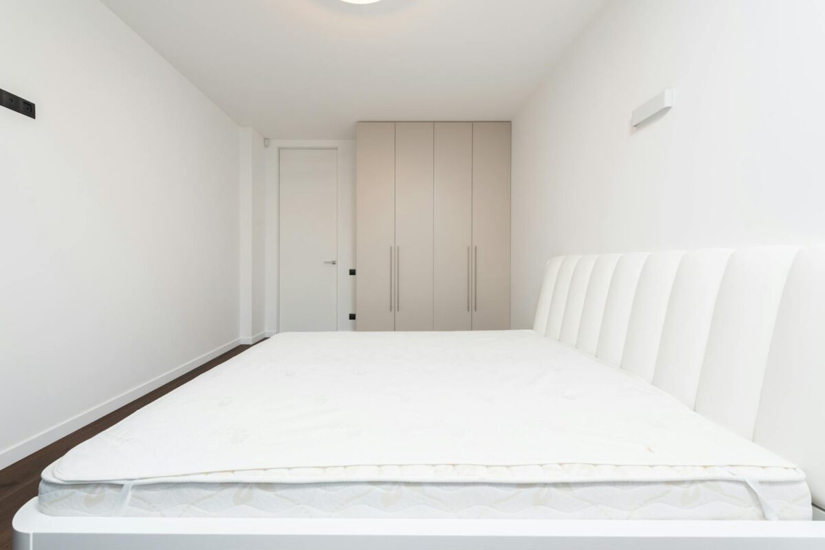 Contemporary minimalist bedroom featuring a white mattress and sleek wardrobe under soft lighting.