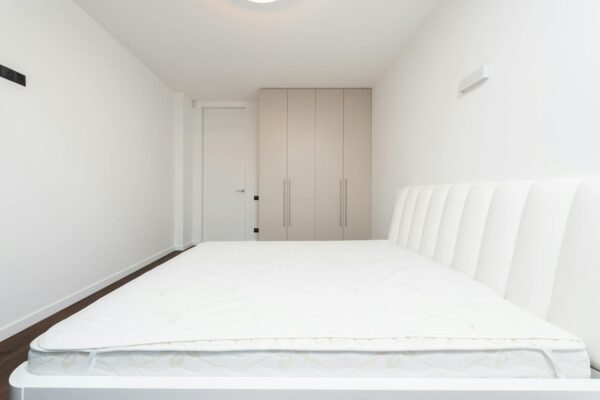 Contemporary minimalist bedroom featuring a white mattress and sleek wardrobe under soft lighting.