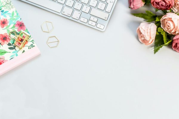 Elegant flat lay of an office desk with floral notebook, roses, and keyboard.