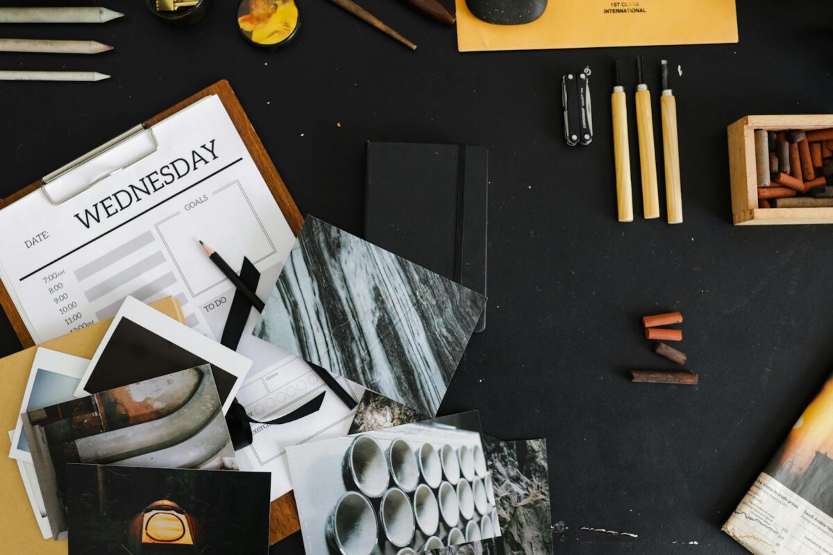 An overhead view of a creative workspace with art supplies, photographs, and a weekly planner.