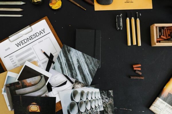 An overhead view of a creative workspace with art supplies, photographs, and a weekly planner.