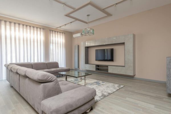 Interior of living room of modern style in beige color with sofa and glass table near TV on wall