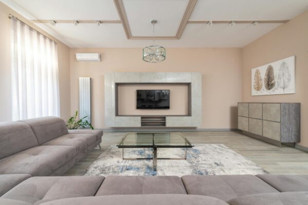 Interior of contemporary living room with glass table and sofa near windows and TV on wall