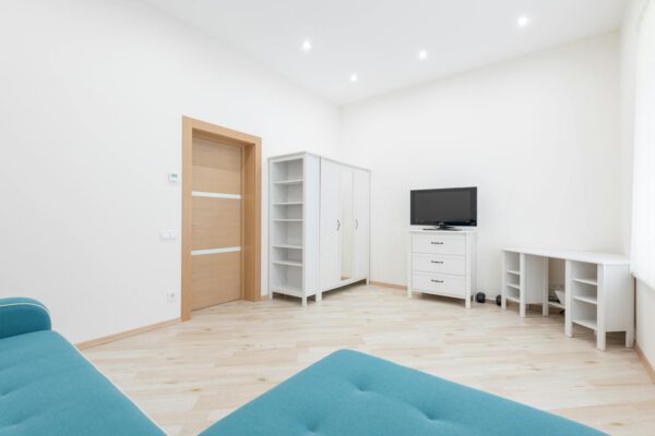 Interior of modern apartment with turquoise couch placed against wall with TV set and white table with closet in apartment