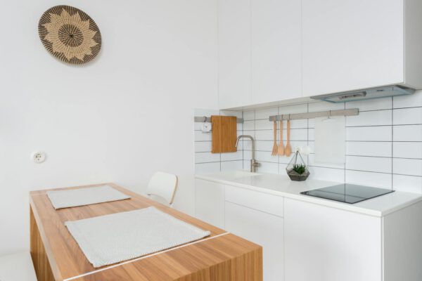 Wooden table with chairs in contemporary kitchen with white cabinets and modern appliances in daylight