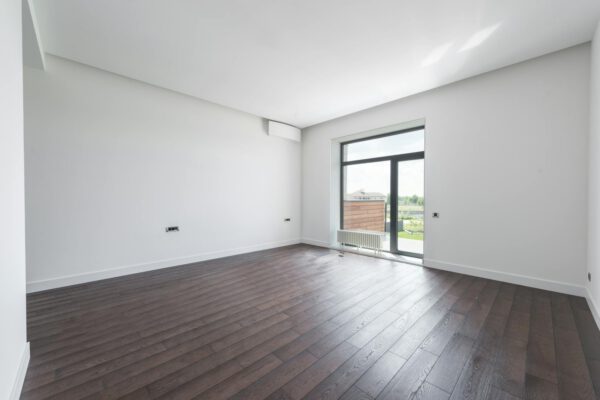 Spacious empty room in new apartment with wooden parquet floor and white wall on sunny day