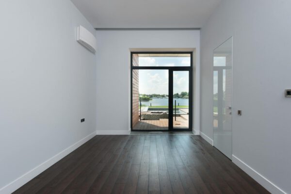 Perspective view of empty spacious hallway with white walls and large window overlooking lake in modern luxury suburban cottage house