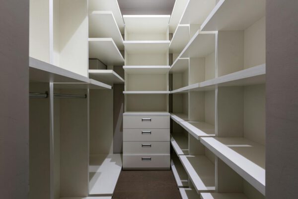 Abundance of empty clean shelves and tall cupboard with metallic handles placed in narrow light modern dressing room at home
