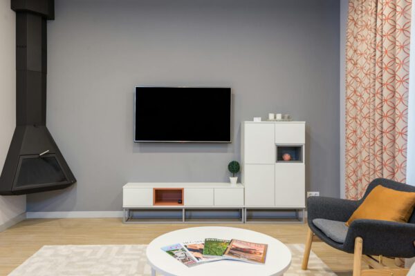 Modern TV and fireplace hanging on wall in minimalist apartment with white furniture and comfortable armchair