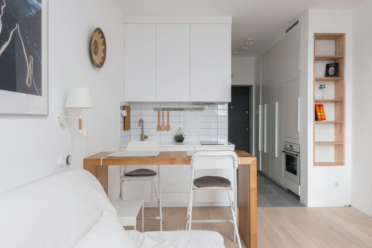 Wooden counter with chairs separating kitchen zone from living room in modern light apartment