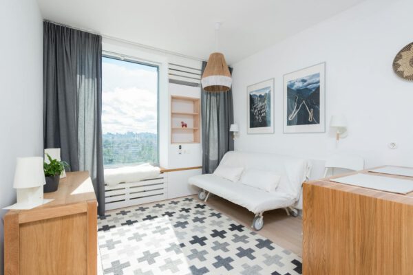 Interior of cozy living room with white walls and sofa placed near wooden table on sunny day in modern apartment