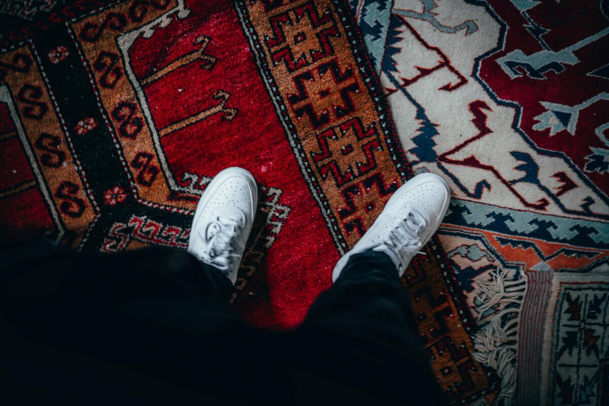 Top view of white sneakers on a colorful patterned rug, emphasizing style and indoors setting.
