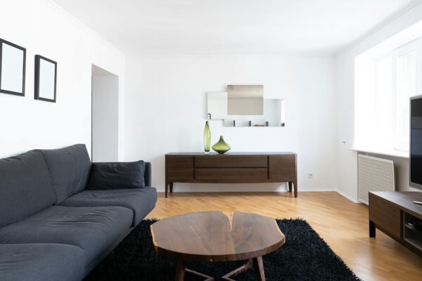Interior of modern light home with couch near wooden table on carpet near cabinets with vases and TV