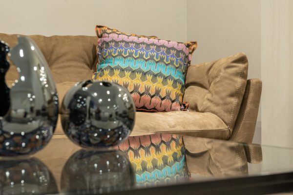 Modern living room interior with comfortable sofa and colorful cushion near table with glass tabletop and shiny decorations