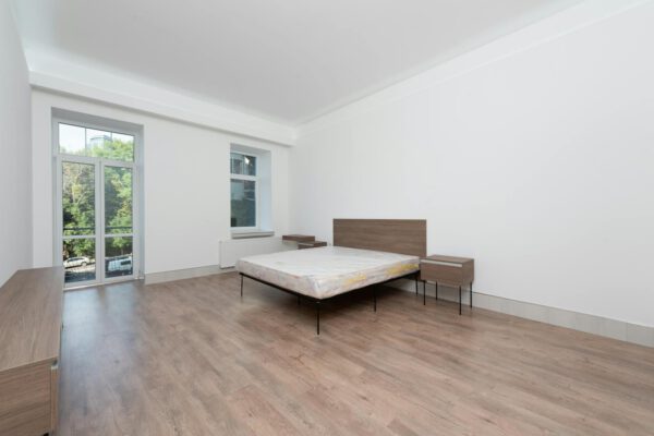 Spacious minimalist bedroom featuring wooden floors and large windows for natural light.