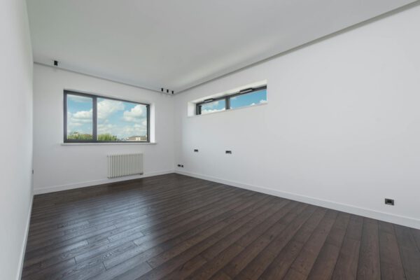 Interior of empty spacious room with laminated floor big windows white walls and ceiling in daylight