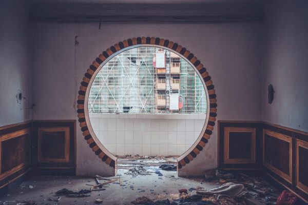 A striking view through a circular window in an abandoned, messy room, revealing urban construction.