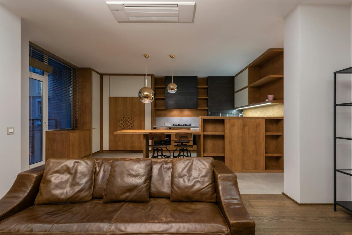 Comfortable leather sofa with pillows in contemporary apartment with modern interior and shelves