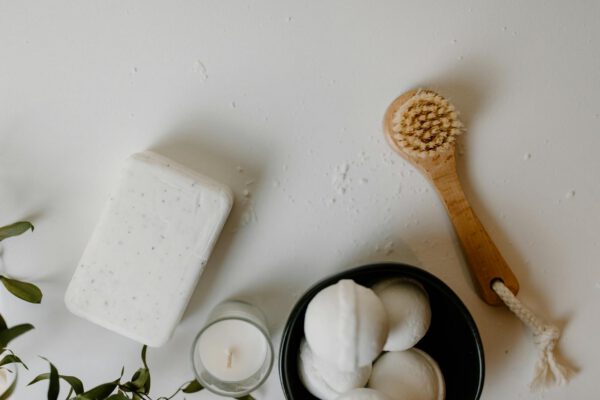A serene flatlay of bath essentials with soap, brush, and candle on white background.