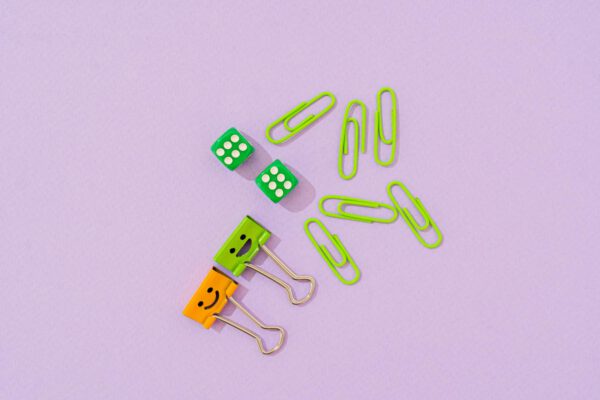 A vibrant assortment of office supplies with binder clips and dice on a purple background.