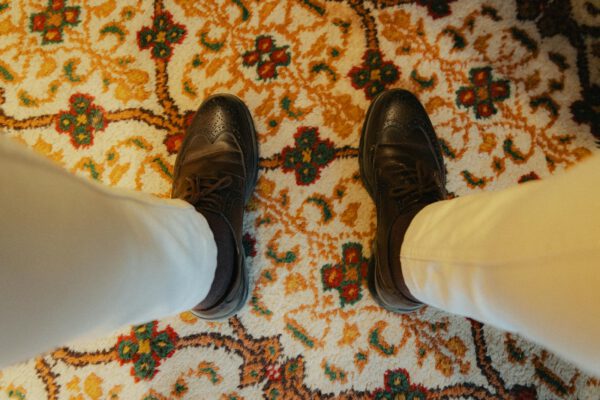 Stylish black leather shoes paired with cream pants on a colorful patterned rug.