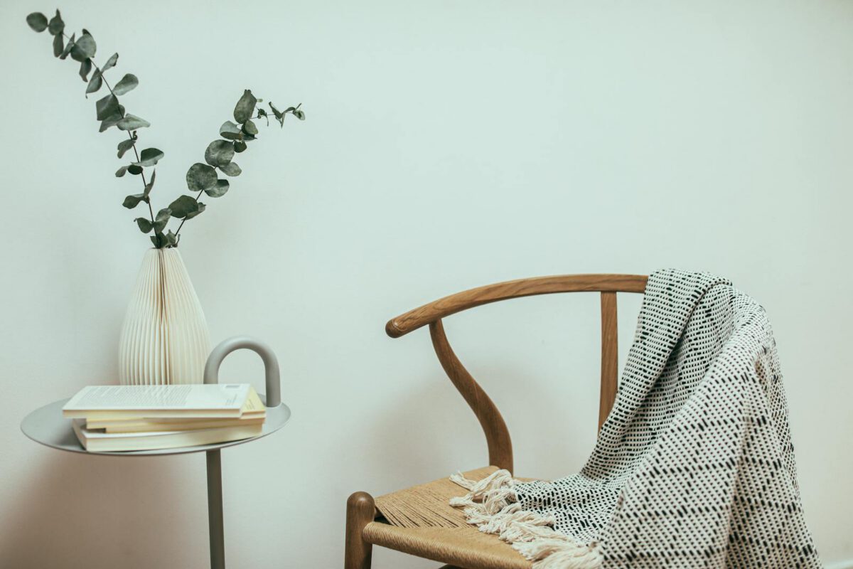 A cozy minimalist corner featuring a wooden chair, blanket, and decorative table.