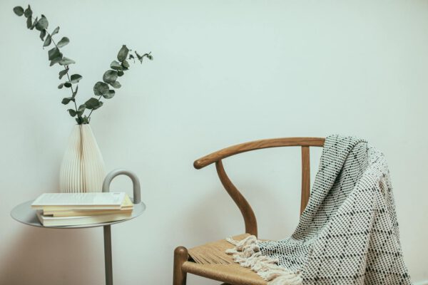 A cozy minimalist corner featuring a wooden chair, blanket, and decorative table.