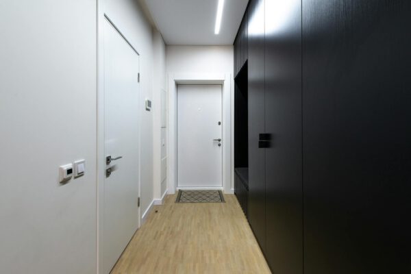 Interior of empty hallway with white doors and black wardrobe under luminous lamp on ceiling