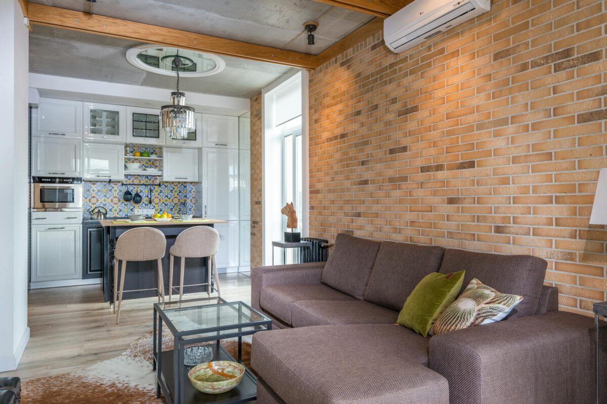Contemporary living room with brick wall, stylish kitchen, and comfortable sofa featuring chic interior design.
