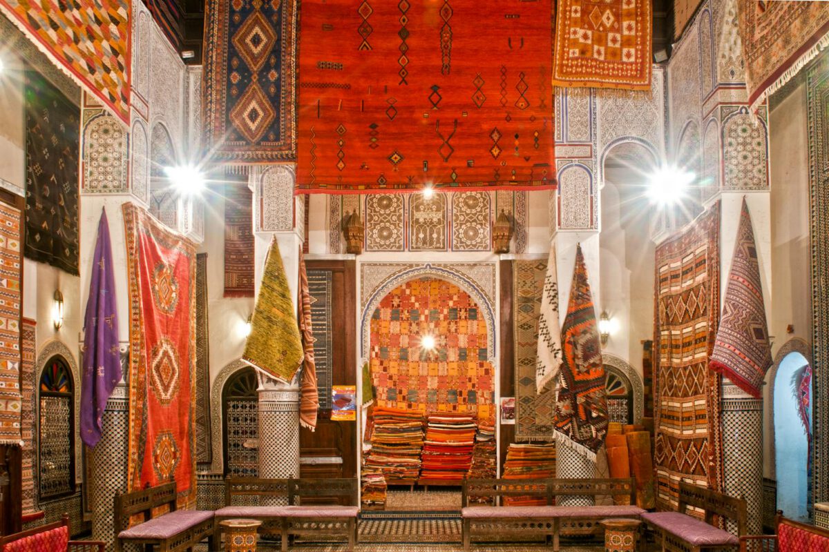 Colorful display of Moroccan rugs in a traditional market in Fès, showcasing intricate patterns and warm tones.