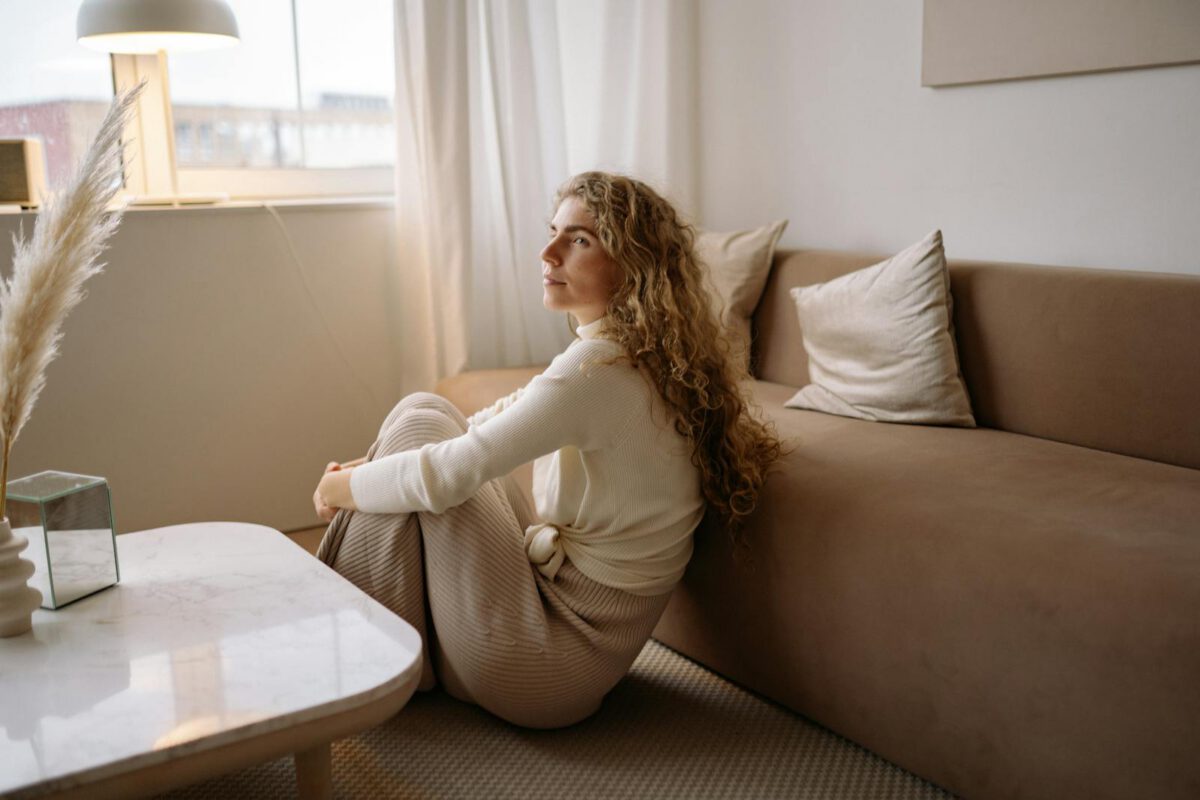A woman with curly hair sits peacefully on the floor of a stylish living room, exuding calm and comfort.