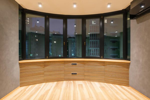 Contemporary empty room with windows and parquet under bright lamps against air conditioning in urban house