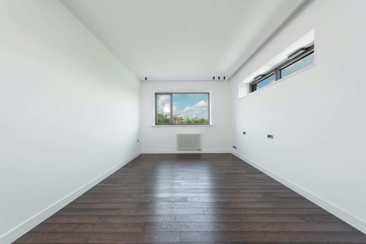 Interior of empty spacious room with white walls and brawn parquet floor in daylight